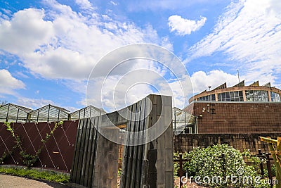 A waterfall over a stone wall with a doorway on a curved footpath in the garden with blue sky and powerful clouds Stock Photo