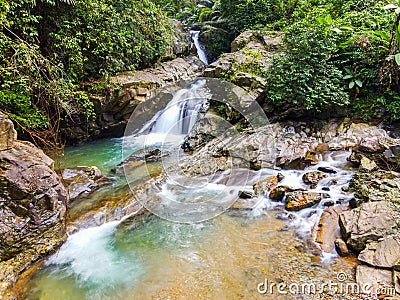 Waterfall with big rock bank in the green tropical forest Stock Photo