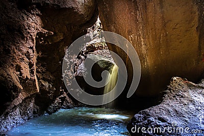 Waterfall of a small stream of fresh water coming out entering a dark cavern rocky brown colors and green moss Stock Photo