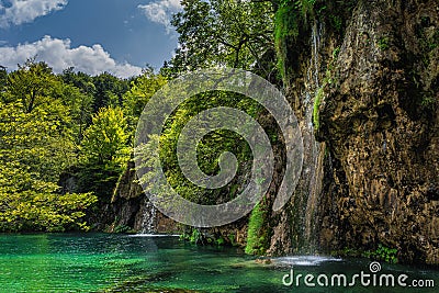 Waterfalls coming down from tall cliffs to turquoise coloured lake in Plitvice Lakes Stock Photo