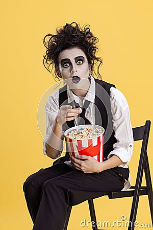 Cropped portrait of creepy looking, expressive woman in Halloween costume holding popcorn basket isolated over yellow Stock Photo