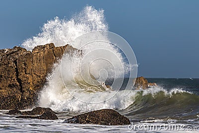 Wave breaking against giant rock offshore, spray high in the air. Stock Photo