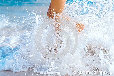 A wave breaks on the shore and the beautiful legs of a young girl. Ocean foam and sea water splashes. Beach holidays Stock Photo