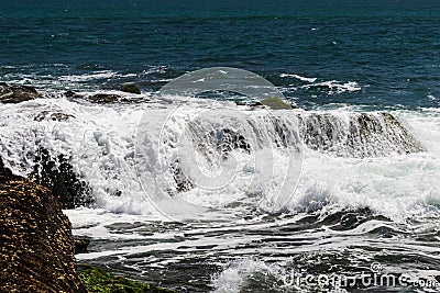 Wave cascading over rocks at low tide; Bali, Indonesia. Stock Photo