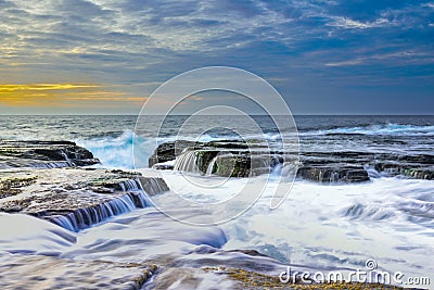 The wave flows over weathered rocks and boulders at North Narrabeen Stock Photo