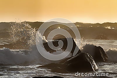 Waves breaking across black rocks on a beach Stock Photo