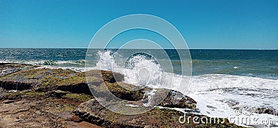 Waves breaking on the rocks on the beach with the sea and blue sky in the background Stock Photo