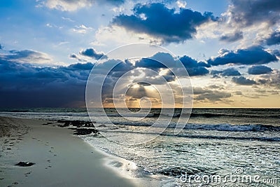 The waves of the Caribbean Sea roll ashore. The rays of the rising sun penetrate the clouds Stock Photo