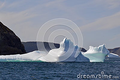 Waves crashing against icebergs stranded next to rugged coastline in bay outside St. John's Stock Photo