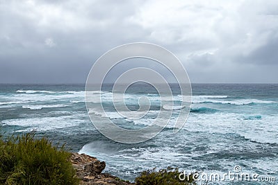 Waves crashing on the rocky coastline with dark ominous clouds Stock Photo