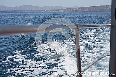 Waves with foam overboard the ship with the coast in the background. Stock Photo