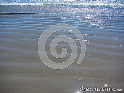 Waves and ripples rolling inshore along a sandy beach Stock Photo