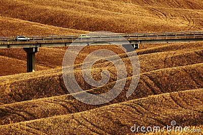 Wavy breown hillocks, sow field, agriculture landscape, bridge with two cars, nature carpet, Tuscany, Italy Stock Photo