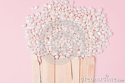 Wax for depilation of white pearl color and wooden stick spatula on pink background. Concept of waxing, smooth skin, bodycare, spa Stock Photo