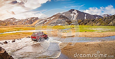 4WD car is crossing a river near major campsite in colorful rainbow volcanic Landmannalaugar mountains with thousands tourists and Editorial Stock Photo