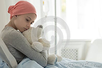 Weak girl with cancer wearing pink headscarf and hugging teddy bear Stock Photo