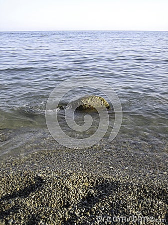 Weak waves gently wash the stones lying on the shallow bottom of the sea rocky shore in good weather Stock Photo