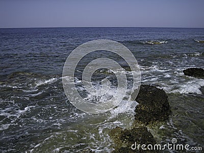 Weak waves gently wash the stones lying on the shallow bottom of the sea rocky shore in good weather Stock Photo