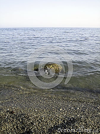 Weak waves gently wash the stones lying on the shallow bottom of the sea rocky shore in good weather Stock Photo