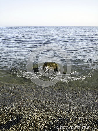 Weak waves gently wash the stones lying on the shallow bottom of the sea rocky shore in good weather Stock Photo