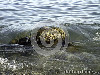 Weak waves gently wash the stones lying on the shallow bottom of the sea rocky shore in good weather Stock Photo