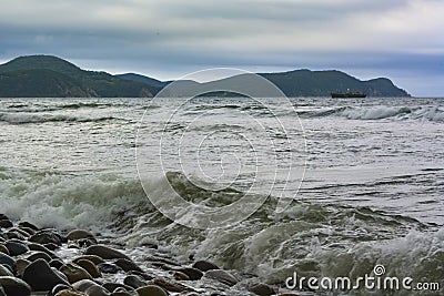 Raging sea after a storm, green mountains and a ship in the distance Stock Photo