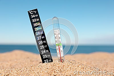 Weather thermometers in sand near sea, closeup Stock Photo