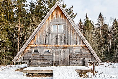 Weathered and aged log cabin surrounded by trees and snow. Stock Photo