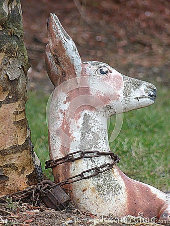 Weathered Lawn Ornament or Statue of a Deer Chained to a Tree with a Rusty Chain and Padlock Stock Photo
