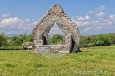 Weathered stone arch of Kilmacduagh Abbey in Galway set against green fields and distant rolling hills Stock Photo