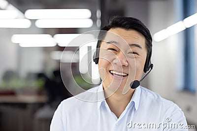 Webcam view, Asian support worker in shirt with headset smiling and looking at camera, businessman working inside office Stock Photo