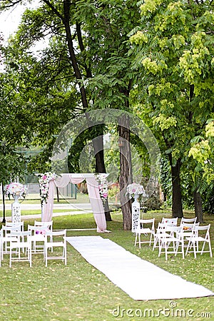 Wedding amazing arch, decorated by roses and chairs in park. Stock Photo