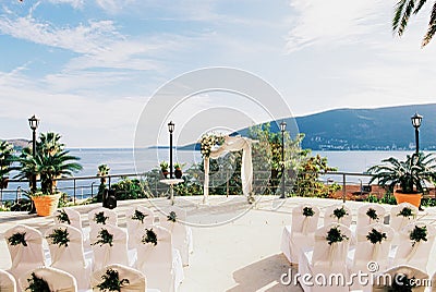 Wedding arch stands on the promenade by the sea in front of the rows of chairs Stock Photo