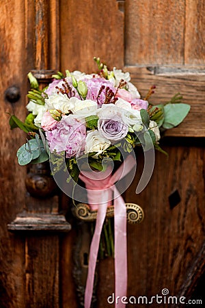 Wedding bouquet hanging on an old door handle on the background of ancient wooden doors. Stock Photo