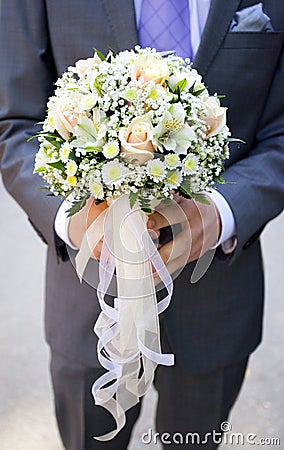 Wedding bouquet of pale pink and yellow flowers and ribbons in hands of groom Stock Photo