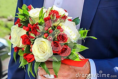 Wedding bouquet of red and white roses and hypericum in the hand of groom. Stock Photo