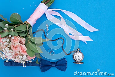 Wedding bouquet and wedding rings on a background of blue paper with a man`s butterfly and an old clock on a chain Stock Photo