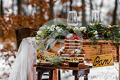 Wedding cake with fruit and an old wooden table with needles of cones and leaves during a wedding ceremony in winter on snow in Stock Photo