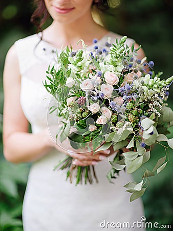 Wedding ceremony. Young bride holds oversized wedding bouquet with blue thistle flowers, jana roses, eucalyptus leaves Stock Photo