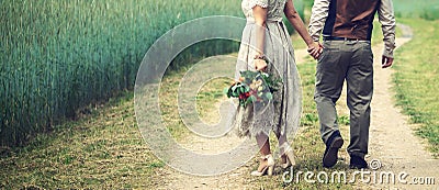 wedding couple, bride and groom holding hands and walks the country road beside cereal field. back view Stock Photo