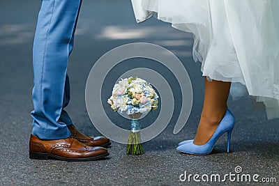 Wedding details: classic brown and blue shoes of bride and groom. Bouquet of roses standing on the ground between them. Newlyweds Stock Photo