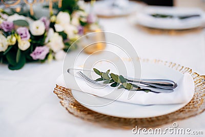 Wedding dinner table reception. White plate on top of a wildcard with golden edges. In a white plate there is a napkin Stock Photo