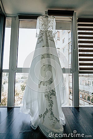 Wedding dress on hanger by the window in the bride room. On her wedding day Stock Photo