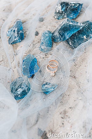 Wedding and engagement rings on a sheer fabric on a beach with decorative blue stones Stock Photo