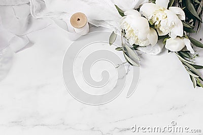 Wedding floral still life composition. Bouquet of white peony flowers, olive branches on marble table with silk cloth Stock Photo
