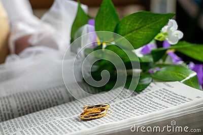 Wedding gold rings on bible with flowers and part of vicar in background Stock Photo