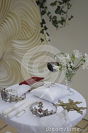 Wedding items: bible, orthodox cross, newlyweds crowns, wedding rings on a cushion, candles, a glass of wine, flowers in a crystal Stock Photo