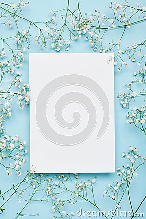 Wedding mockup with white paper list and flowers gypsophila on blue background from above. Beautiful floral pattern. Flat lay. Stock Photo