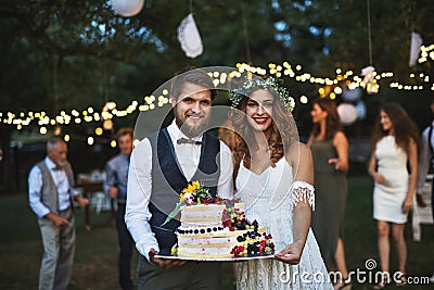 Bride and groom holding a cake at wedding reception outside in the backyard. Stock Photo