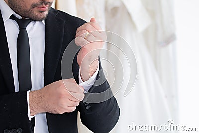 Wedding shopping for man concept, handsome man in tuxedo with beard fasten the buttons in fitting room, groom button up his shirt Stock Photo